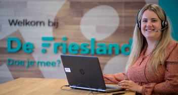 Medewerker De Friesland zit aan bureau achter de laptop. Op de achtergrond: Welkom bij De Friesland.