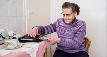 Mevrouw Jongsma aan de keukentafel met een daisyspeler